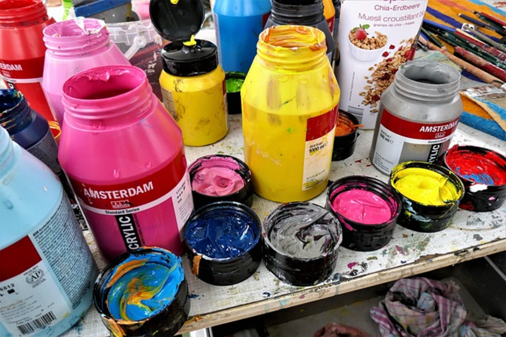 Plusieurs pots de gouaches étalés sur une table.