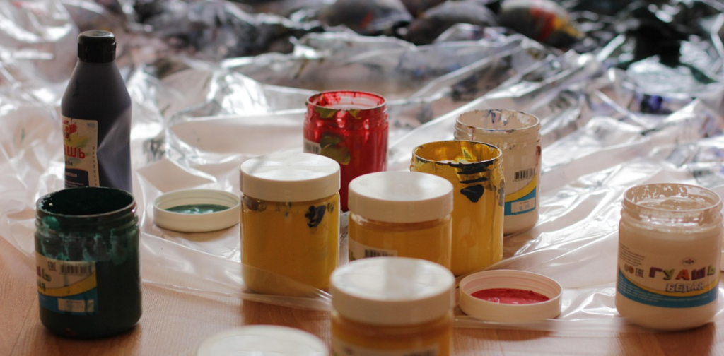 Plusieurs pots de peinture étalés sur le sol avec une toile de plastique afin de le protéger.